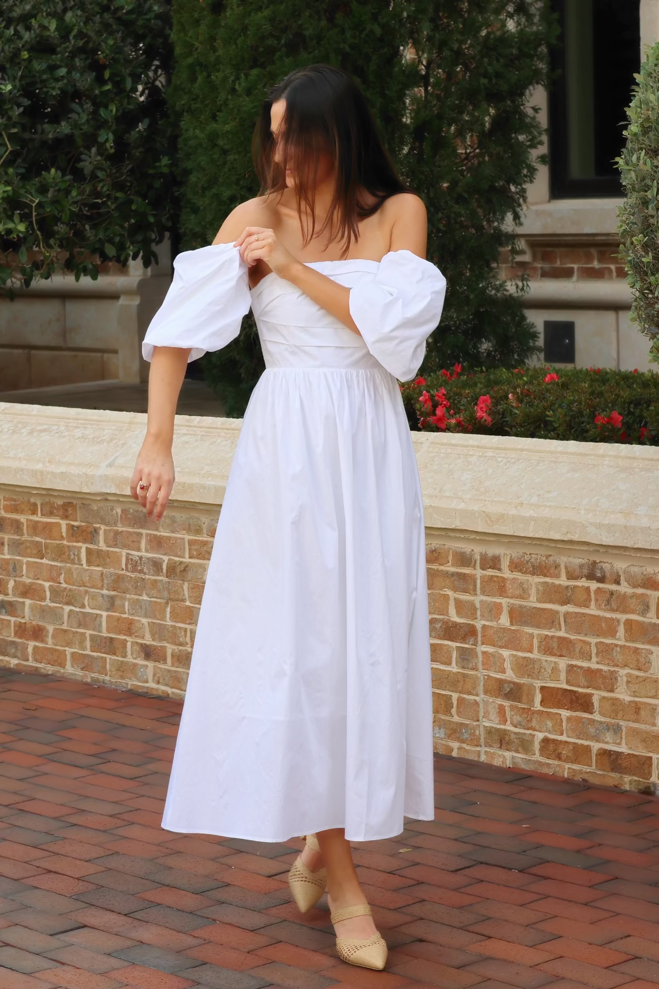 Woman in a white dress standing on a brick path with greenery in the background